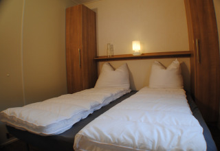 Deux lits simples avec couettes blanches dans un lodge compact au Lodge at Camping Roland aux Pays-Bas.