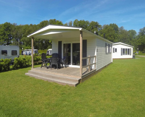 Lodge moderne avec terrasse en bois couverte, mobilier de jardin et pelouse verte, près d’autres lodges.