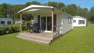 Lodge moderne avec terrasse en bois couverte, mobilier de jardin et pelouse verte, près d’autres lodges.