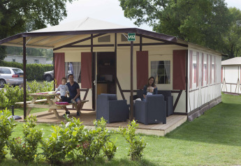 Famiglia rilassata fuori dal lodge Vakwerktent al Camping Roland, circondata dal verde nei Paesi Bassi.