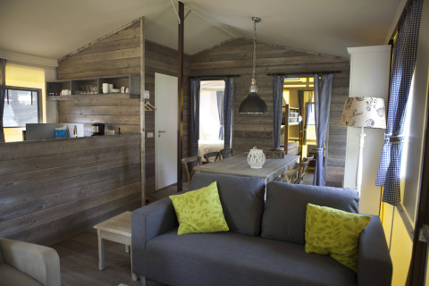 Interior acogedor de cabaña de madera en Vakwerktent, Camping Roland, Países Bajos, con sofá y comedor.