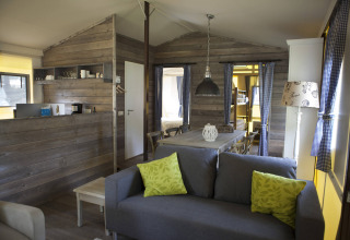 Interior acogedor de cabaña de madera en Vakwerktent, Camping Roland, Países Bajos, con sofá y comedor.