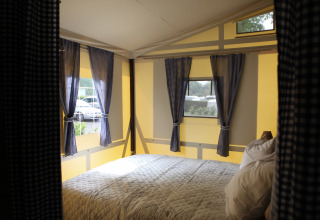 Vista interna di un letto accogliente con tende a quadretti in una Vakwerktent al Camping Roland, Paesi Bassi.
