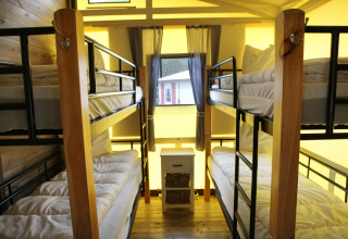 Stanza con quattro letti a castello e dettagli in legno nella Vakwerktent lodge al Camping Roland, Paesi Bassi, con finestra.