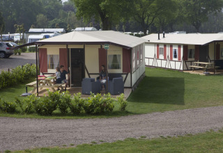 Feriehytter på Camping Roland i Holland med terrasse, havemøbler og afslappede feriegæster i solen.