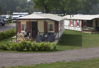 Feriehytter på Camping Roland i Holland med terrasse, havemøbler og afslappede feriegæster i solen.