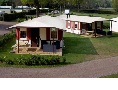 Deux lodges Vakwerktent au Camping Roland aux Pays-Bas, entourés de verdure et équipés de tables extérieures.