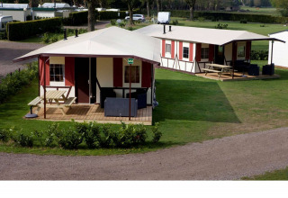 Deux lodges Vakwerktent au Camping Roland aux Pays-Bas, entourés de verdure et équipés de tables extérieures.