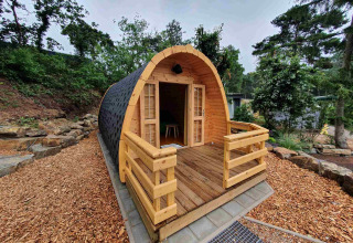 Pequeña casa de madera llamada Pod en Camping Roland, Países Bajos, con terraza y rodeada de naturaleza.