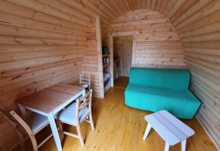 Interior de una pequeña casa de madera, Pod, con mesa de comedor, sofá y mesa en Camping Roland, Países Bajos.