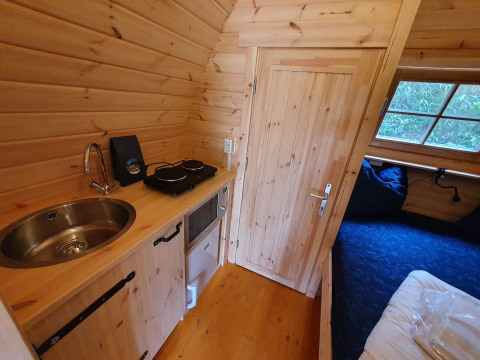 Vista interior de una pequeña casa pod de madera con cocina y cama en Camping Roland, Países Bajos.