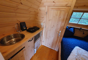 Vista interior de una pequeña casa pod de madera con cocina y cama en Camping Roland, Países Bajos.