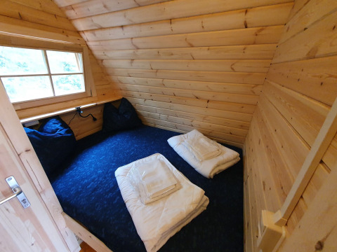 Acogedor dormitorio en una pequeña casa de madera Pod en Camping Roland, Países Bajos, con cama y ventana.