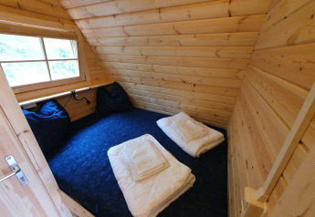 Acogedor dormitorio en una pequeña casa de madera Pod en Camping Roland, Países Bajos, con cama y ventana.