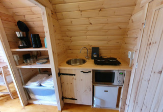 Pequeña cocina en una cabaña de madera con fogones, fregadero, cafetera, microondas y mini nevera.