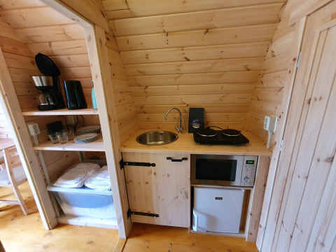 Pequeña cocina en una cabaña de madera con fogones, fregadero, cafetera, microondas y mini nevera.