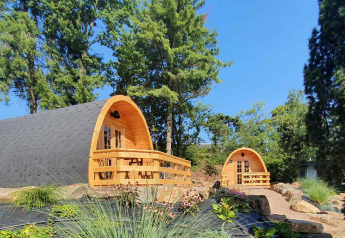 Deux petites maisons en bois nommées Pods dans un jardin verdoyant entouré d’arbres sous ciel bleu.