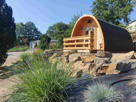 Pequeña casa de madera llamada Pod en Camping Roland, Países Bajos, rodeada de rocas y vegetación.
