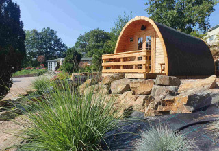 Pequeña casa de madera llamada Pod en Camping Roland, Países Bajos, rodeada de rocas y vegetación.
