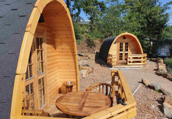 Cabañas tipo pod de madera con pequeñas terrazas en Camping Roland, Países Bajos, rodeadas de árboles.