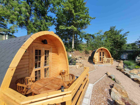Dos pequeñas casas de madera tipo pod en Camping Roland, Países Bajos, rodeadas de árboles y senderos.