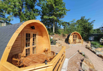 Dos pequeñas casas de madera tipo pod en Camping Roland, Países Bajos, rodeadas de árboles y senderos.