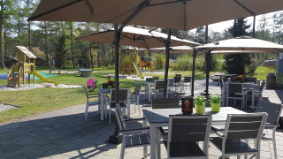 Zona de asientos al aire libre con mesas, sillas y sombrillas grandes, parque infantil al fondo en Drenthe, Países Bajos.