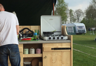 Cocina exterior en el Stoere Safari tent de Camping de Berghoeve, Países Bajos, con hombre cocinando.