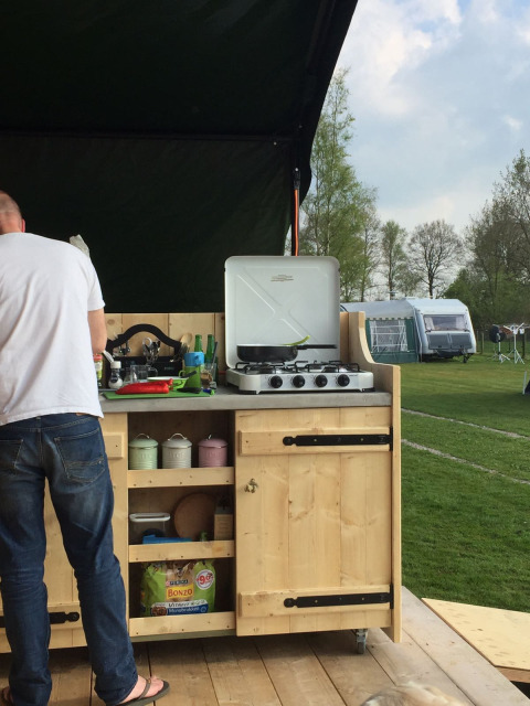Outdoor kitchen at Stoere Safari tent, Camping de Berghoeve, Netherlands, with man cooking and green field.
