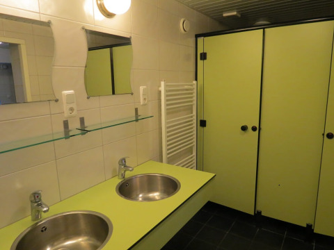 Moderne badkamer bij een glampingaccommodatie met twee spoelbakken, spiegels en groene cabines.