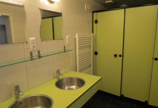Modern bathroom at a glamping site featuring two sinks, mirrors, green-colored stalls, and tiled walls.