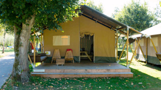 Buitenfoto van een Safari tent lodge met houten veranda, stoelen en een rustige groene omgeving.
