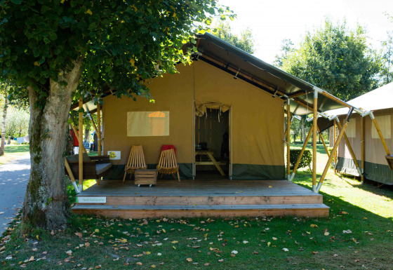 Foto exterior de una tienda tipo Safari lodge con porche de madera, sillas y un entorno natural tranquilo.