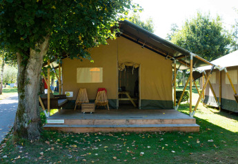 Foto all'aperto di una lodge tenda Safari con veranda in legno, sedie e tranquillo ambiente naturale.