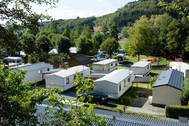 Blick auf den Campingplatz Camping Val d'Or in Wiltz, Luxemburg, umgeben von Bäumen und Hügeln.