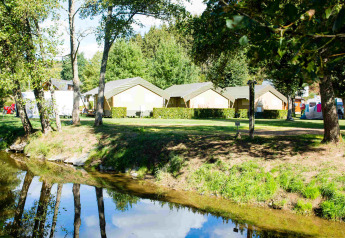Safari tents at Camping Val d'Or in Luxembourg, seen by a small creek and surrounded by greenery and trees.