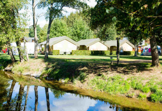 Safari-Zelte auf dem Campingplatz Val d'Or in Luxemburg, von Bäumen und einem kleinen Fluss umgeben.