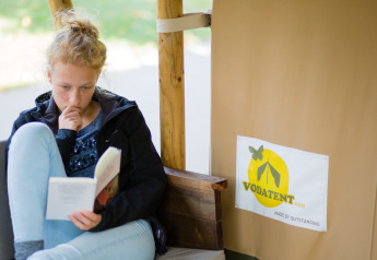 En pige læser en bog i en safaritelt-lodge på Camping Val d'Or i Luxembourg, ved siden af Vodatent-logoet.