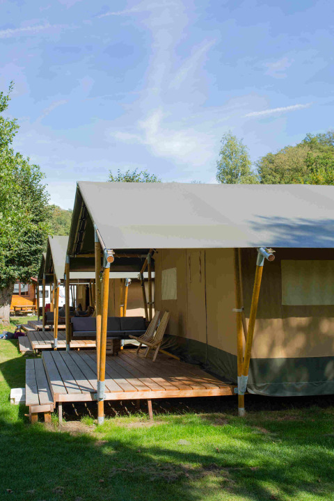 Safaritelt på Camping Val d'Or i Luxembourg, træterrasse og stole under en blå himmel.