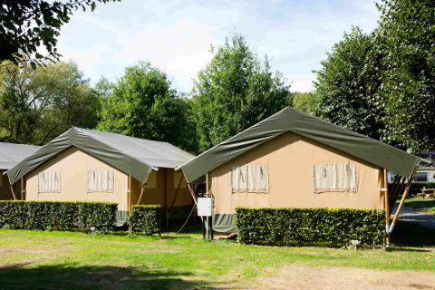 Two safari tents at Camping Val d'Or in Luxembourg, surrounded by hedges and trees on a sunny day.