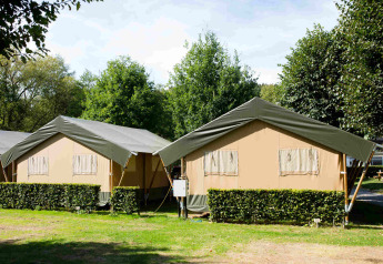 Zwei Safarizelte auf dem Campingplatz Val d'Or in Luxemburg, umgeben von Bäumen und grünen Hecken.