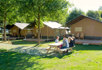 Picknicktafel en safaritenten op Camping Val d'Or in Luxemburg, mensen genieten van het buitenleven.