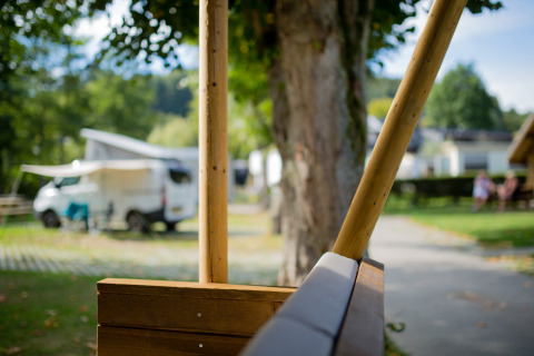 Blick von einer Holzbank auf einen Wohnwagen und grüne Umgebung im Camping Val d'Or in Luxemburg.