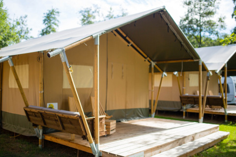 Safari-Zelt auf dem Campingplatz Val d'Or in Luxemburg, mit Holzterrasse und Bank im Grünen.