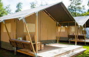 Safari-Zelt auf dem Campingplatz Val d'Or in Luxemburg, mit Holzterrasse und Bank im Grünen.