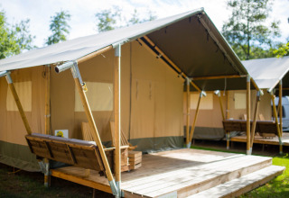 Tienda safari en Camping Val d'Or, Luxemburgo, con terraza de madera y banco, rodeada de árboles.