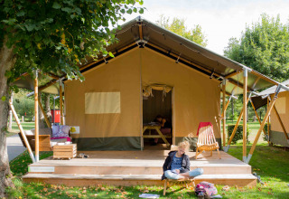 Tienda safari en Camping Val d'Or, Luxemburgo, con niños relajándose en la terraza de madera bajo un árbol.