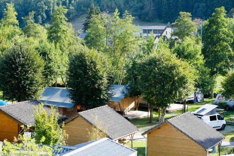 Safari-Zelte und Holzhütten auf Camping Val d'Or in Luxemburg, umgeben von Bäumen und Natur.