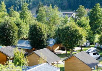 Safari tenten en houten huisjes bij Camping Val d'Or in Luxemburg, omringd door groen en bomen.