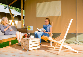 Two people relaxing outside a safari tent at Camping Val d'Or in Luxembourg, enjoying drinks and reading.